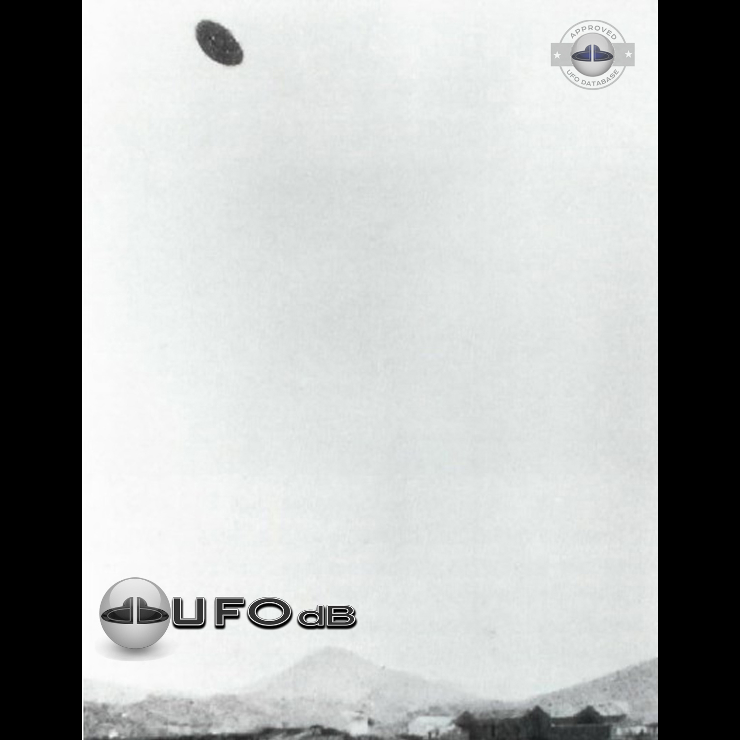 Grey UFO picture UFO high in the sky over buildings and mountains UFO Picture #106-1